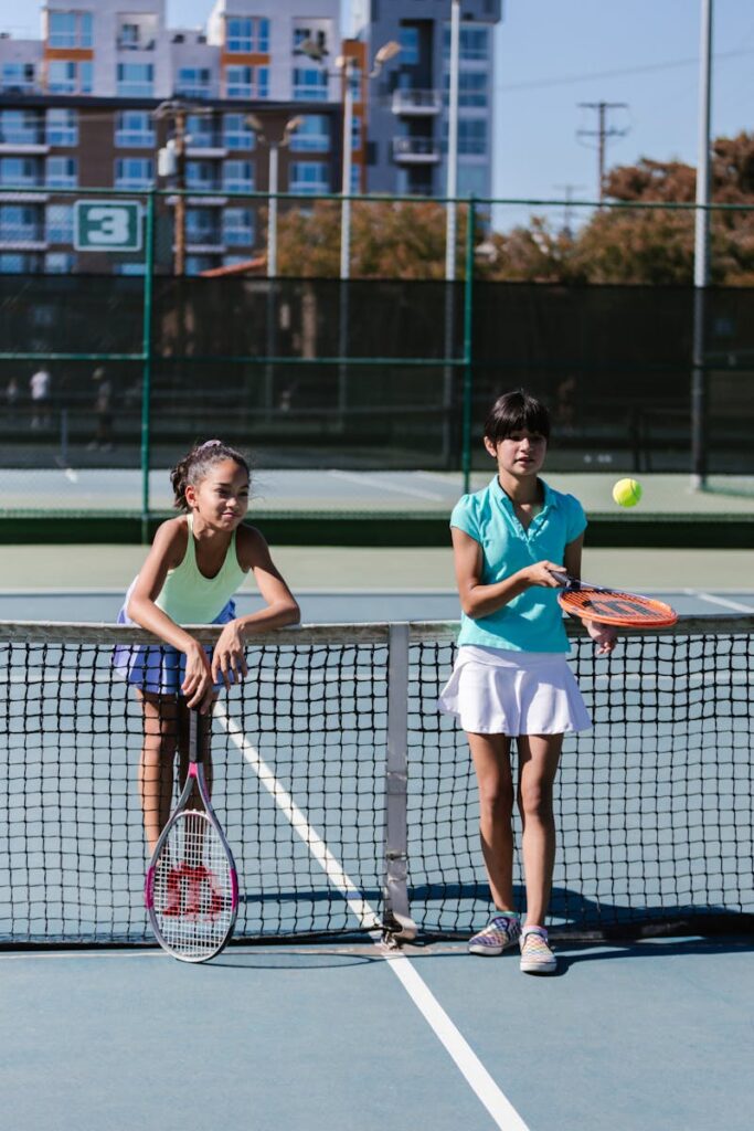 Two girls in sportswear play tennis on an outdoor court, enjoying the game.
