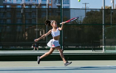 Young girl in activewear playing tennis on a sunny day outdoors.